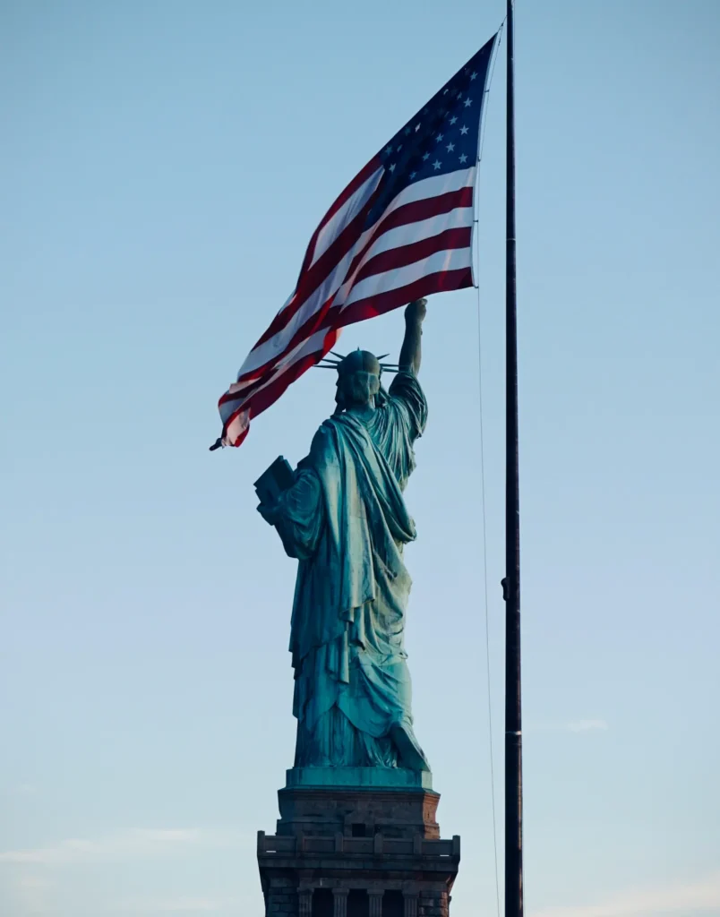 The Statue of Liberty with a U.S. flag behind it.